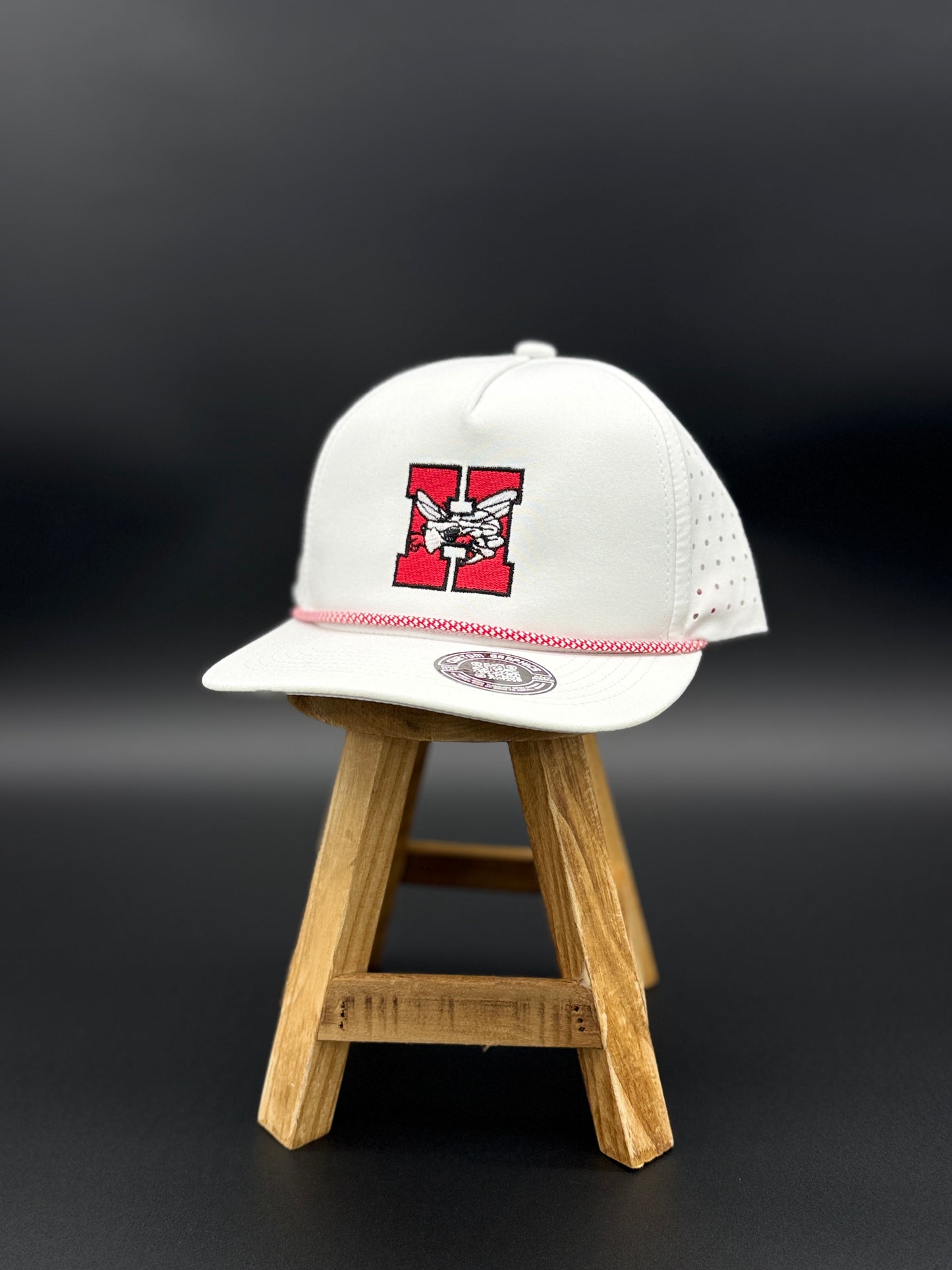 White Hilldale H embroidered cap with red and black design by Cuztom Graphics displayed on wooden stand
