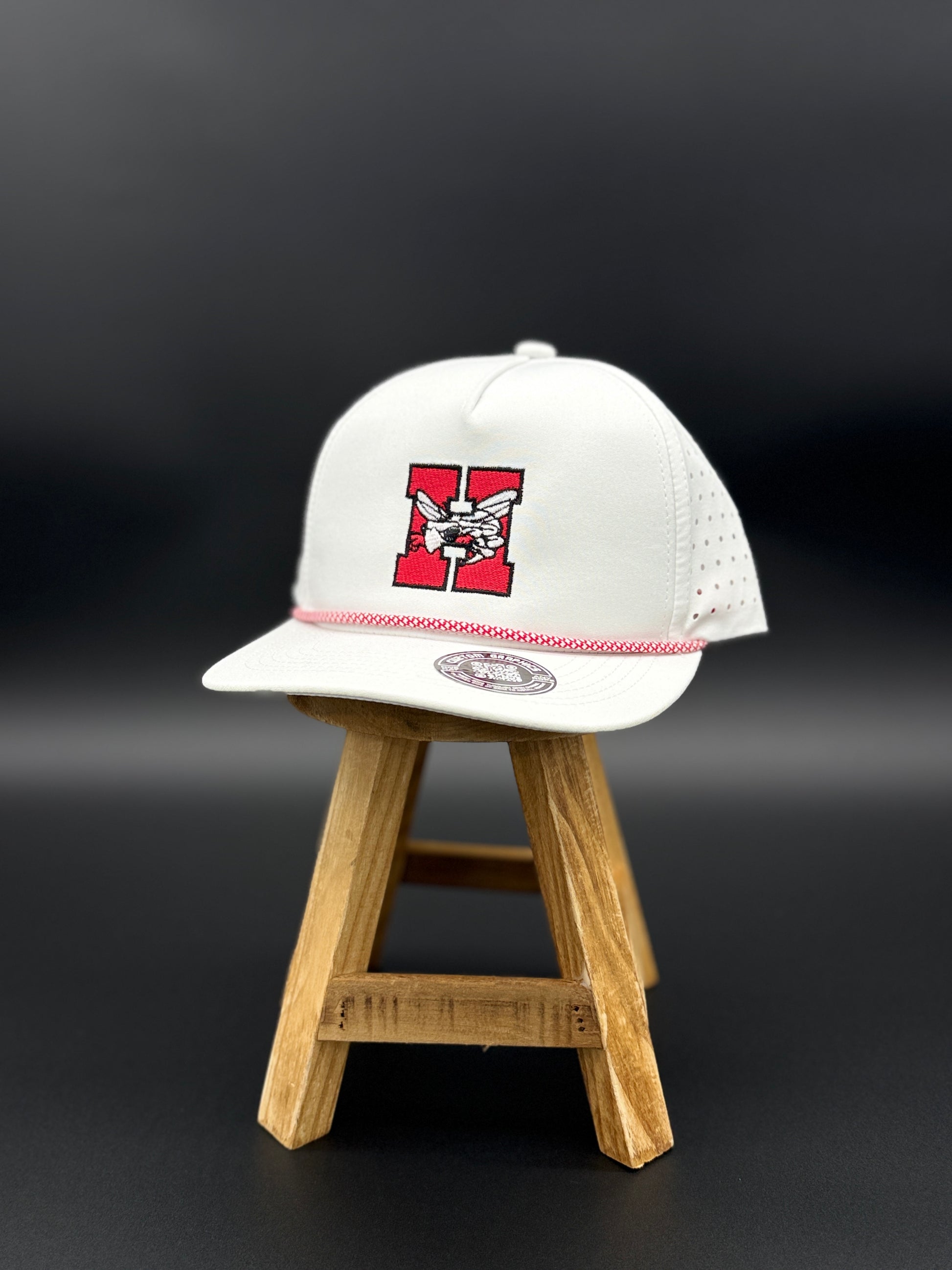 White Hilldale H embroidered cap with red and black design by Cuztom Graphics displayed on wooden stand
